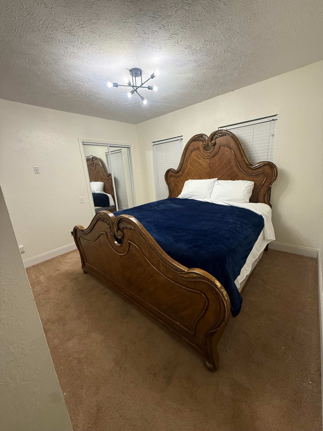 The king bedroom, with a carved wooden headboard and footboard, a navy blanket folded over white bedding, and a mirrored closet.
