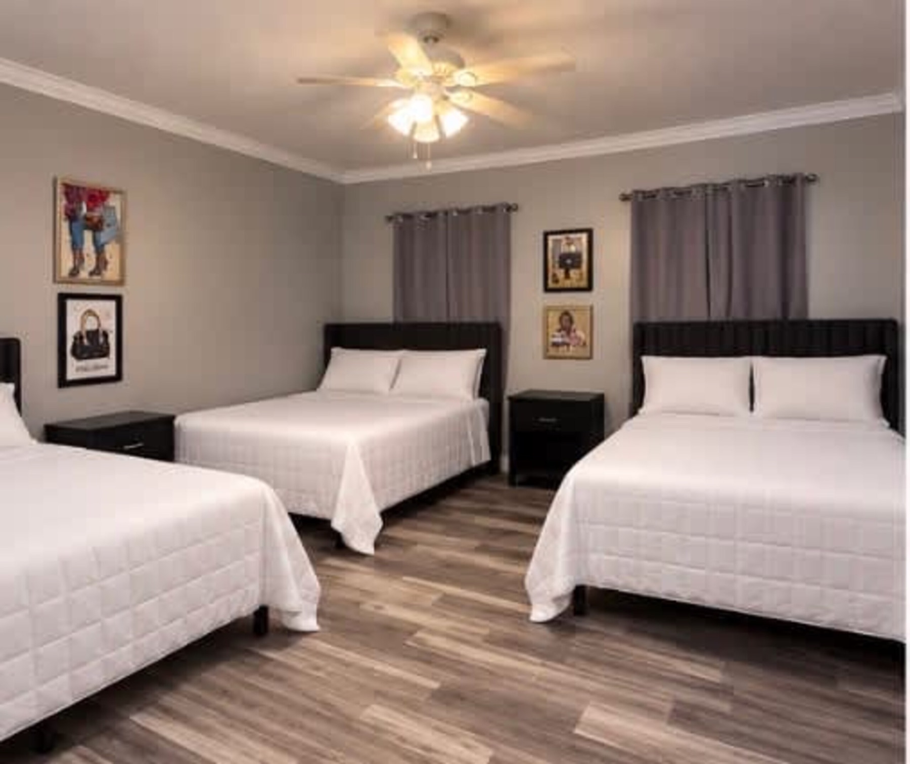 A bedroom with three full beds against grey walls, black upholstered headboards, white bedding and framed art.