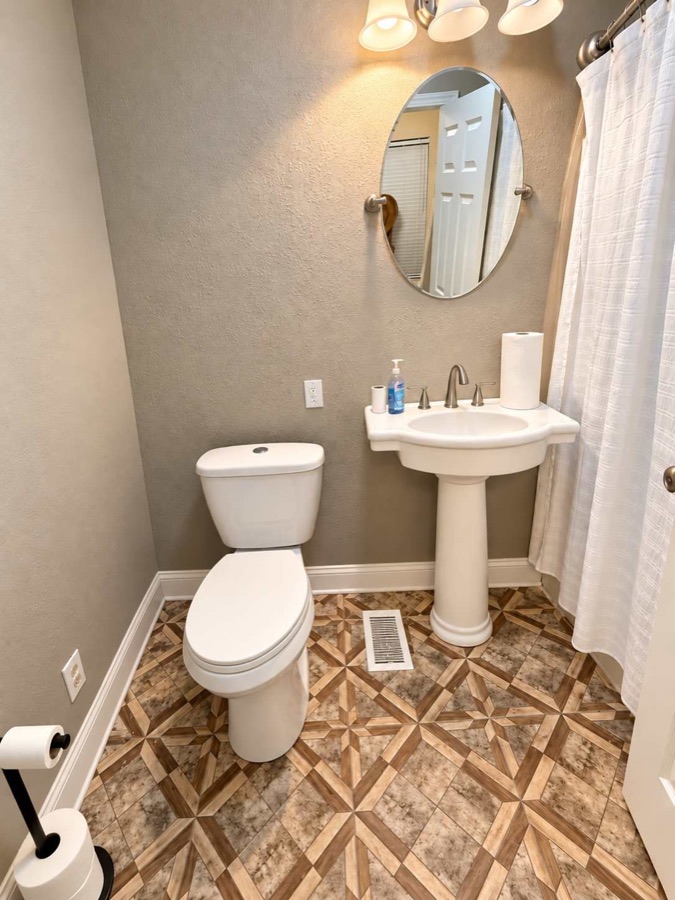 A half bathroom with a pedestal sink, oval mirror and patterned tile floor.