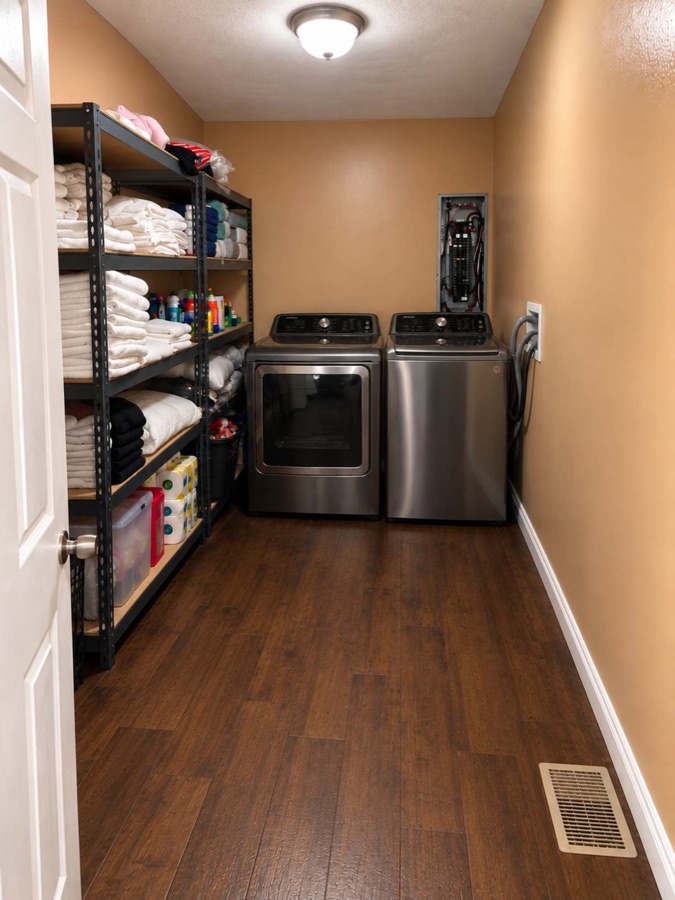 The laundry room: a full-size washer and dryer beside steel shelving stacked with folded white towels and household supplies.