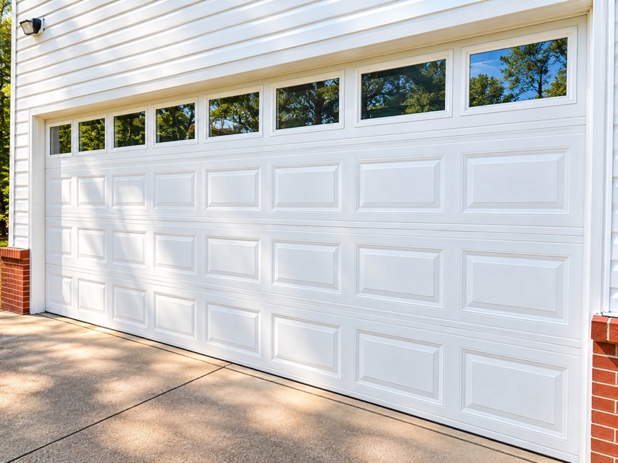 A white double garage door set into the brick and siding, with a concrete apron in front of it.